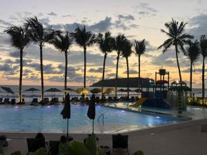 a pool with palm trees and a sunset in the background at Viaggio Resort Mazatlán in Mazatlán