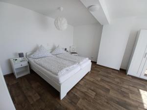 ein weißes Schlafzimmer mit einem weißen Bett und einem Holzboden in der Unterkunft Lütje Huus in Upgant-Schott