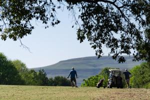 Due uomini che camminano in un campo con una golf cart di Gooderson Monks Cowl Golf Resort a Champagne Valley