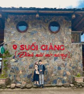 a couple standing in front of a stone building at Không gian văn hóa trà Suối Giàng in Văn Chấn