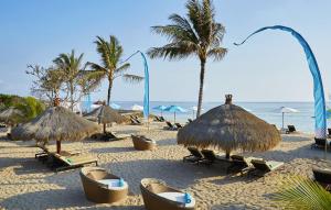 a beach with chairs and straw umbrellas and palm trees at SOL by Meliá Benoa Bali All inclusive in Nusa Dua