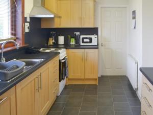 a kitchen with wooden cabinets and a sink and a microwave at Cluaran Cottage in Tain