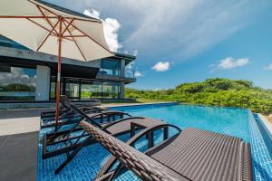 a pool with chairs and an umbrella next to a house at Castello do mare カステロディマーレ in Miyako Island
