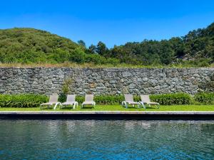 four chairs sitting next to a rock wall next to a body of water at Quinta da Boa Viagem in Viana do Castelo