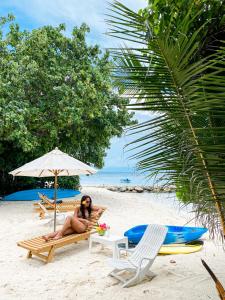 a woman sitting on a beach under an umbrella at Summer Vibes Beach Front in Rasdhoo