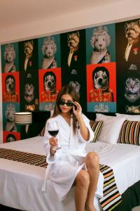Mood Hotel Lifestyle في تشيكلايو: امرأة تجلس على سرير مع كوب من النبيذ