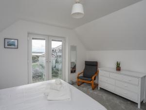 een witte slaapkamer met een bed en een stoel bij 9 Lon Y Dryw in Holyhead