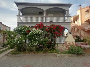 a house with red and white flowers on a fence at Apartmani kod Rade in Pakoštane