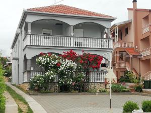 a house with a balcony with red and white flowers at Apartmani kod Rade in Pakoštane
