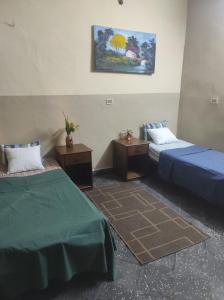 Zimmer mit 2 Betten, 2 Tischen und einem Gemälde in der Unterkunft Hostal Jardín de Luque in San Lorenzo