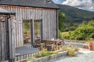 Cuillrigh - Luxury house, loch & mountain views في بورتري: كابينة خشبية مع طاولة وكراسي في الخارج