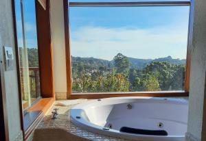 uma banheira na casa de banho com uma grande janela em Chalés Mirante Monte Verde em Monte Verde