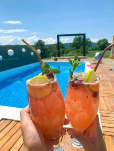 a person holding two cocktails in their hands near a pool at Skriveni raj in Gornji Milanovac