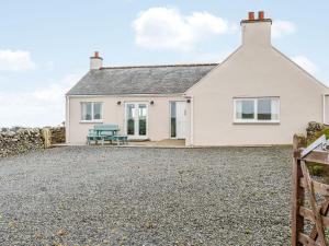 a white cottage with a bench on a gravel driveway at Auld Dairy Cottage in Drummore