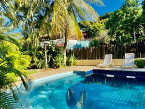 a swimming pool with two chairs and a palm tree at Pousada Refugium in Itacaré
