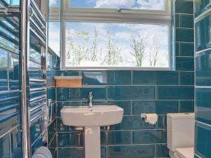 een blauw betegelde badkamer met een wastafel en een raam bij Ty Haf in Roch