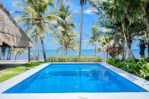 a swimming pool with palm trees and the ocean at Villa Tankah Mandala in Tulum