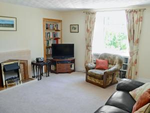 sala de estar con sofá, TV y silla en Old Midoxgate Farmhouse, en Calrossie