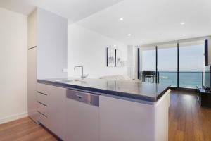 a white kitchen with a sink and a view of the ocean at Arena Newcastle Beach in Newcastle