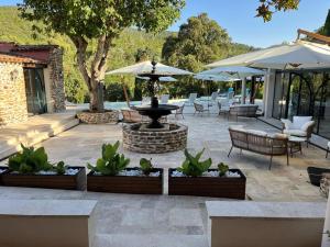 un patio con una fuente, sillas y sombrillas en Auberge du dom en Bormes-les-Mimosas