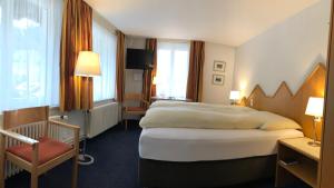 una habitación de hotel con una cama grande y una silla en Hotel Weisses Kreuz Bergün en Bergün