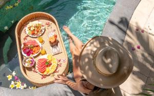 una persona en un sombrero sentada junto a una mesa con comida en The Oberoi Luxury Villas Seminyak, en Seminyak
