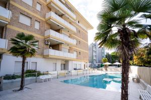 a swimming pool in front of a building with palm trees at Benelux in Lido di Jesolo