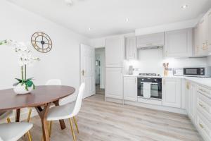 Skye Sands - City Road Residence - Central St Andrews في سانت أندروز: مطبخ بدولاب بيضاء وطاولة وكراسي خشبية