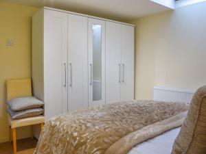 a bedroom with white cabinets and a bed and a chair at The Stables At Early Autumn in Eynsford