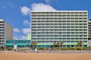 Holiday Inn Va Beach-Oceanside 21st St, an IHG Hotel في فرجينيا بيتش: مبنى طويل مع أشجار النخيل أمام الشاطئ