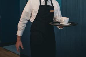 a man holding a tray with a cup and a coffeeucer at Hotel Royal Continental in Naples