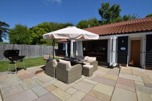 un patio con mesa, sombrilla y sillas en Woodland Lodge, Aldeburgh, en Aldeburgh