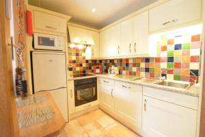a kitchen with white cabinets and colorful tiles on the wall at Seafarers in Fressingfield