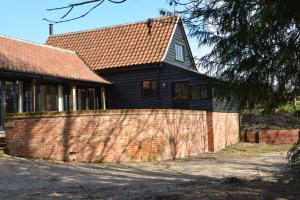 a black house with a brick wall in front of it at Bird Cottage, Burgh in Grundisburgh