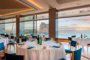 a restaurant with white tables and chairs and windows at Hotel Royal Continental in Naples