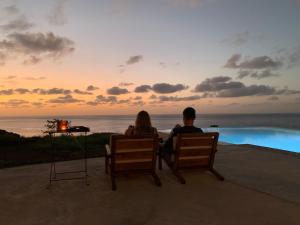 Ein Mann und eine Frau sitzen auf Stühlen und beobachten den Sonnenuntergang. in der Unterkunft Palmeira Da Cruz EcoLodge in Chã da Igreja