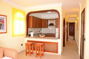 una cocina con armarios de madera y una barra con taburetes en Apartamentos Callaomar, en Callao Salvaje