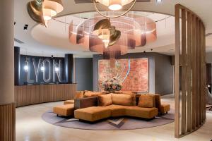 a lobby with a couch and a large chandelier at NH Lyon Airport in Saint-Exupéry