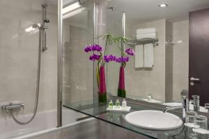 a bathroom with a sink and a glass counter with purple flowers at NH Lyon Airport in Saint-Exupéry