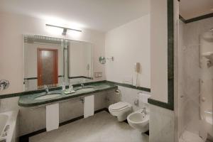 a bathroom with two sinks and a toilet and a mirror at NH Lecco Pontevecchio in Lecco