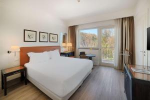 um quarto de hotel com uma grande cama branca e uma janela em NH Catania Parco degli Aragonesi em Catânia