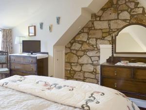 a bedroom with a stone wall with a bed and a dresser at The Wee Hoose in Kinghorn