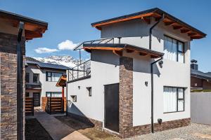 a white house with a balcony and mountains in the background at Cabañas El Aby in El Bolsón
