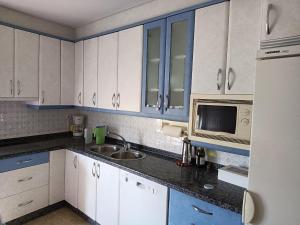 cocina con armarios blancos, fregadero y microondas en CASA ABUELA, en Palacios de la Valduerna