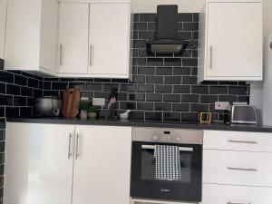 een keuken met witte kasten en een zwarte tegelmuur bij 2 Bedroom House next to Slade Green Station in Slades Green