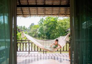 a man laying in a hammock on a porch at Ban Sainai Resort- SHA Extra Plus Aonang's Green Resort in Ao Nang Beach