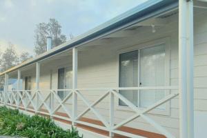 a white house with a wooden railing on a porch at White Cottage on Ninety Mile Beach in Seaspray