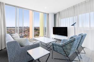 een woonkamer met een bank en stoelen en een tv bij Meriton Suites Zetland in Sydney