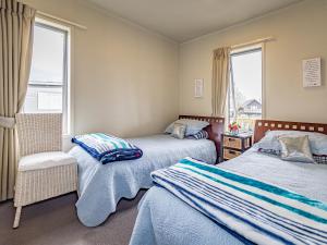 ein Schlafzimmer mit zwei Betten und einem Stuhl und zwei Fenstern in der Unterkunft Alpine Way Cottage - Ohakune Holiday Home in Ohakune