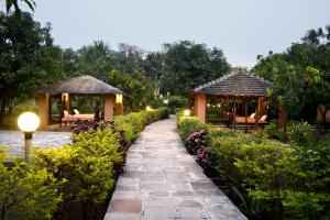 a walkway in a garden with two gazebos at SaffronStays Mango Huts by the River, Pali in Jambhulpāda